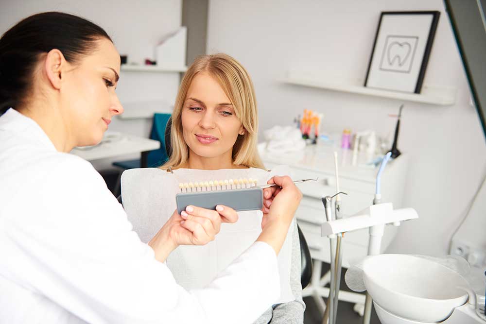 female dentist and young woman choosing the colour