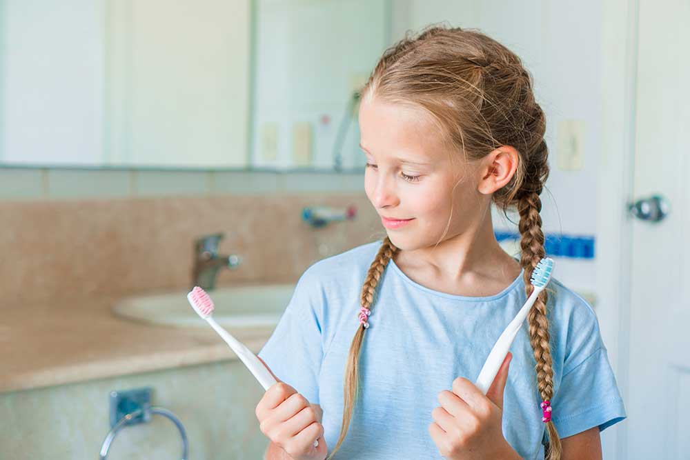 little girl looking at a pink tooth brush